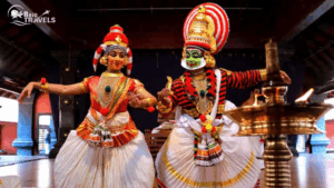 Two Kathakali performers in vibrant traditional costumes dancing on stage, showcasing Kerala’s classical art and cultural heritage, with a brass lamp in the foreground.